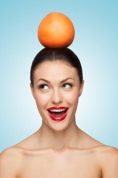 A beautiful young lady with bare shoulders holding a juicy orange on her head.