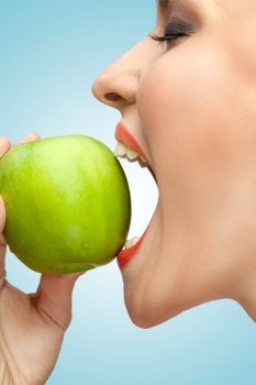 A portrait of a woman biting a green apple with her mouth wide open.