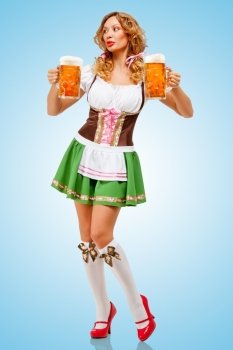 Young sexy Oktoberfest woman wearing a traditional Bavarian dress dirndl serving two beer mugs on blue background.
