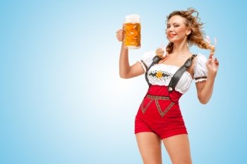 Young flirting sexy Swiss woman wearing red jumper shorts with suspenders in a form of a traditional dirndl, holding a beer mug on blue background.