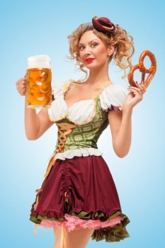 Young sexy Oktoberfest waitress wearing a traditional Bavarian dress dirndl serving a pretzel and beer mug in a tavern on blue background.