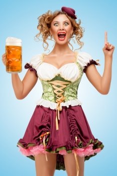 Young sexy Oktoberfest waitress wearing a traditional Bavarian dress dirndl holding a beer mug, and having an idea, on blue background.