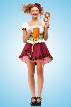 Young sexy Oktoberfest waitress, wearing a traditional Bavarian dress dirndl and serving a pretzel and beer mug in a tavern on blue background.