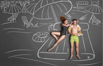 Love story concept of a romantic couple lying on an air mattress against chalk drawings background. Male listening to the music in the headphones and reading a book, female trying to gain his attention.