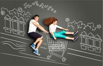Happy valentines love story concept of a romantic couple on chalk drawings background. Male riding his girlfriend in a shopping cart along the street.