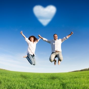 Happy couple jumping in green field against blue sky. Summer vacation concept