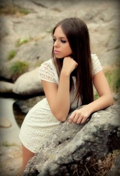 Attractive young woman with white dress posing on a rock