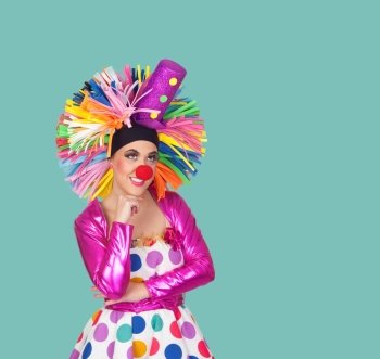 Pensive girl clown with a big colorful wig on green background