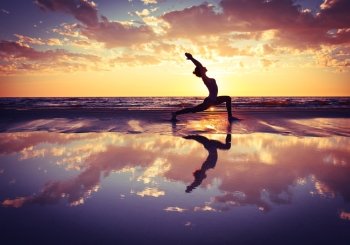 woman practicing yoga . silhouette of woman practicing yoga on the beach at sunset