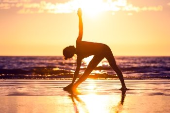 woman practicing yoga . silhouette of woman practicing yoga on the beach at sunset