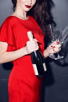 brunette in red dress with bottle of champagne and two glasses. woman in red dress wich champagne