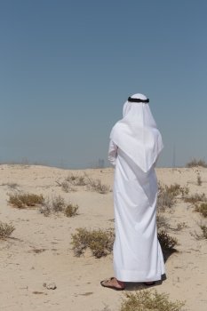 Arab man in national dress stands in the desert and looks at the city of Dubai. Arab man in the desert