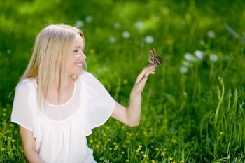 Beautiful blond woman playing with butterfly in spring park