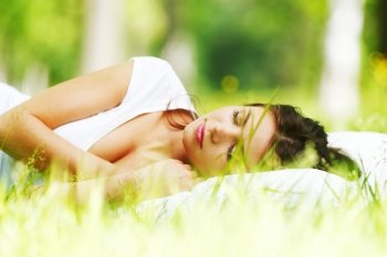 Young woman sleeping on white pillow in fresh spring grass
