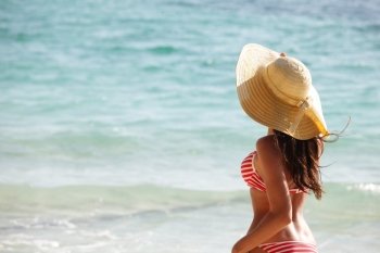 Woman on beach . Woman in sunhat and bikini standing on ocean beach on hot summer day