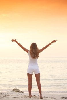 Woman enjoy sunset over sea. Woman standing on beach with raised hands enjoying sunset over sea