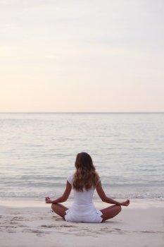 Yoga at sunrise. Woman in lotus yoga pose at sunrise on the beach