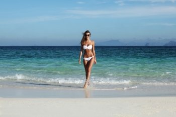 Beautiful fit woman in bikni walking from sea to tropical beach. Woman walk to beach