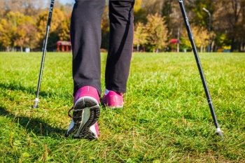 Nordic walking adventure and exercising concept - woman hiking, legs and nordic walking poles in summer nature