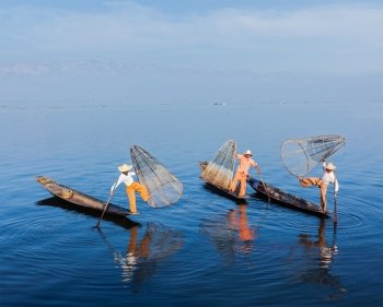 Myanmar travel attraction landmark - Traditional Burmese fishermen balancing with fishing net on boats at Inle lake in Myanmar famous for their distinctive one legged rowing style