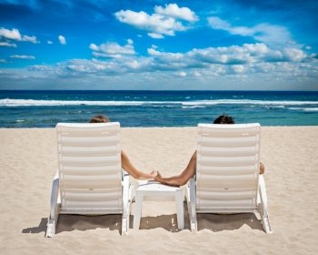 Honeymoon travel resort concept - couple in beach chairs holding hands near ocean