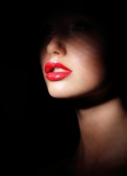Darkness. Woman's Face with Sexy Red Lips in Spotlight and Shadows. Secrecy