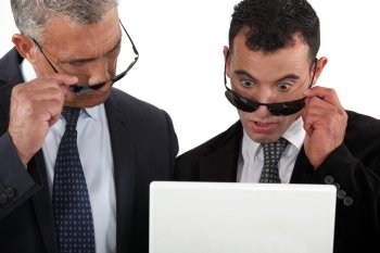 Two businessman taking their sunglasses to look at a laptop.
