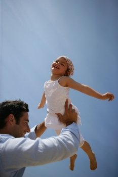Father lifting his daughter against a blue sky