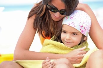 Mother drying daughter with towel at the beach