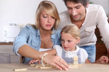 A cute little girl playing dominos with her parents.