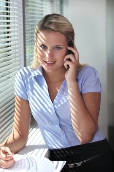Blond office worker making telephone call whilst stood by window