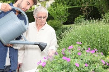 young man watering plants with older woman