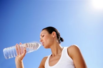 Woman drinking a bottle of water against a blue sky