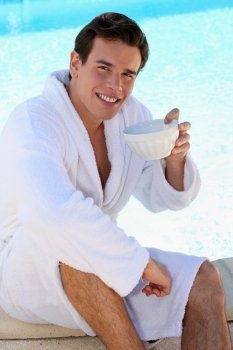 young guy having coffee at edge of swimming-pool