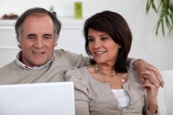 mature couple sitting on sofa with laptop