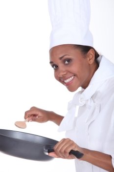 Female chef in uniform with a deep frying pan and wooden spoon