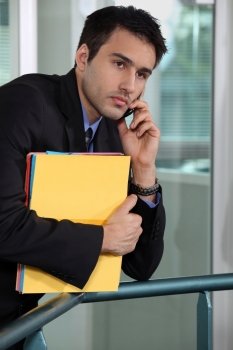 Serious businessman talking on his mobile phone and holding files