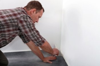 Man fitting linoleum flooring into the corner of a room