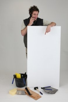 Tiler using cellphone and pointing to poster