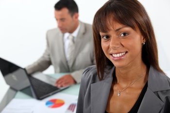 Smiling businesswoman standing in front of a colleague and his laptop