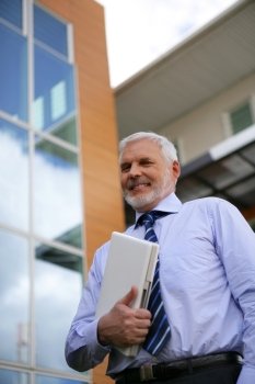 Senior businessman holding laptop outdoors