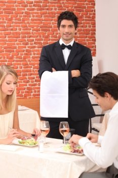 Waiter stood by couple enjoying meal