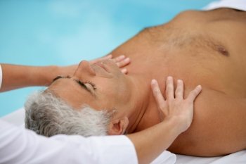 Mature man being massaged next to a swimming pool