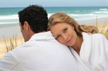 A man and a woman wearing dressing gowns on a beach.