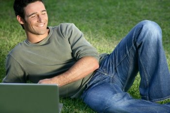 Happy man sat in field with laptop