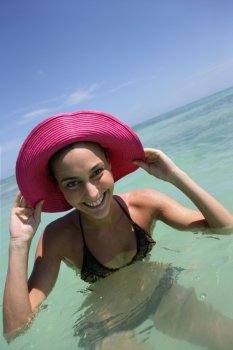 beaming young woman bathing with hands to her sun hat