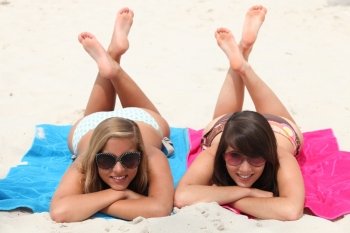 Lazy day on the beach: two girls lying on their stomachs with legs crossed