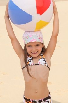 Little at the beach holding inflatable ball above head