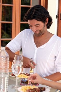 Man opening a bottle of wine at an outdoor lunch