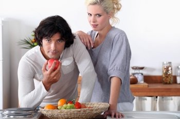 a couple in the kitchen, the man is eating an apple